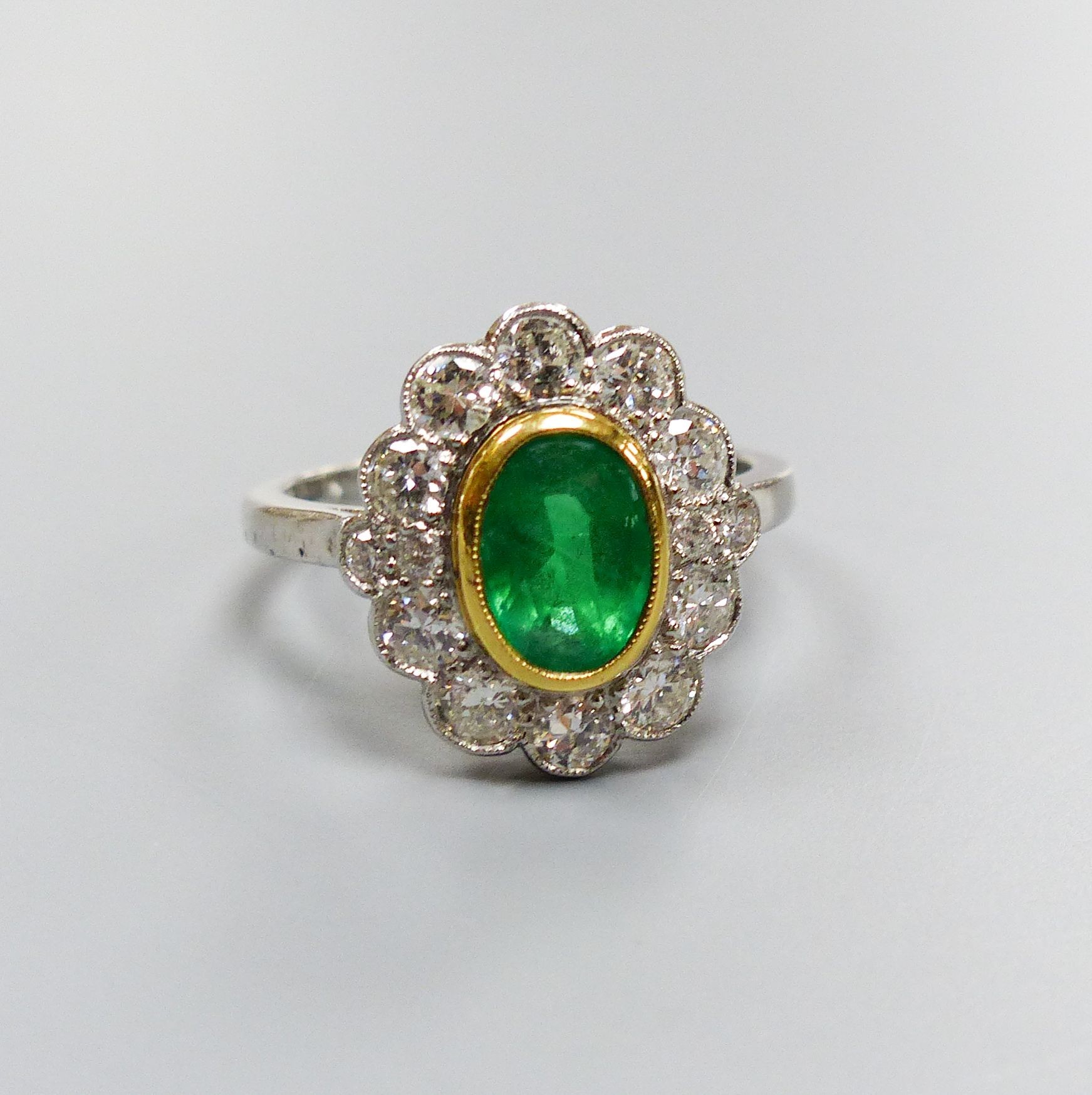 A modern platinum, emerald and diamond set oval cluster ring, size M, gross weight 5.2 grams.